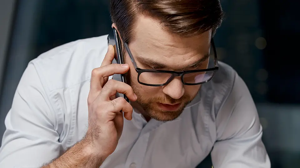 Young adult male with glasses talking on his cell phone at night.